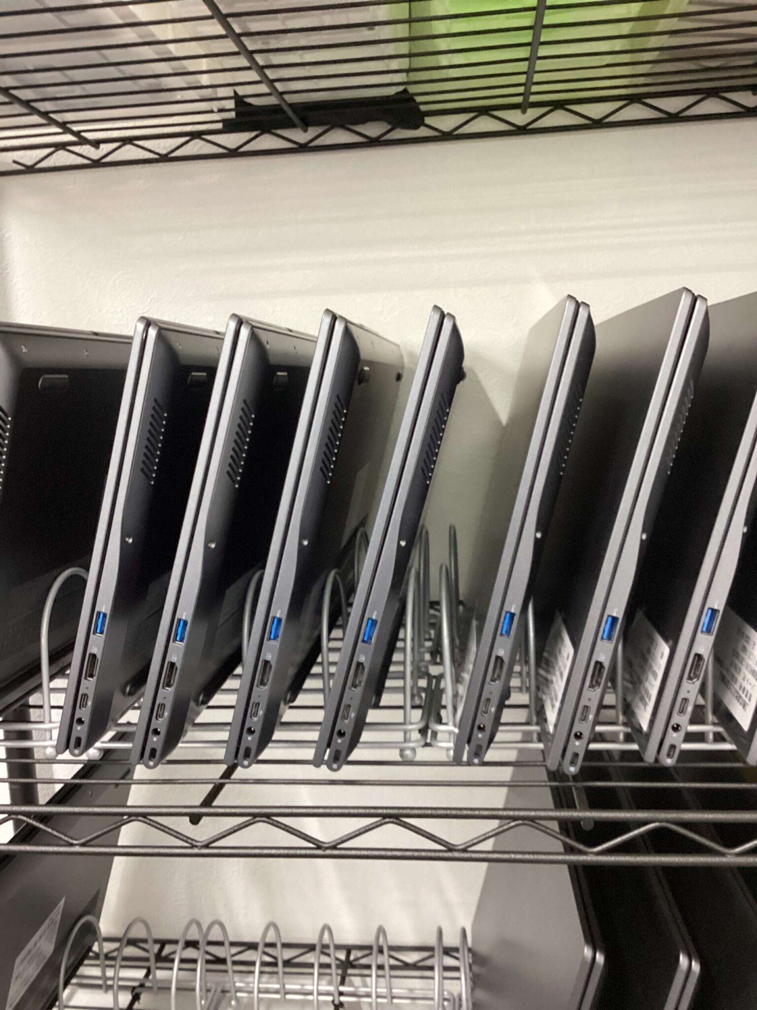 Row of upright docking stations or laptop stands mounted in a metal rack, angled in a storage unit.