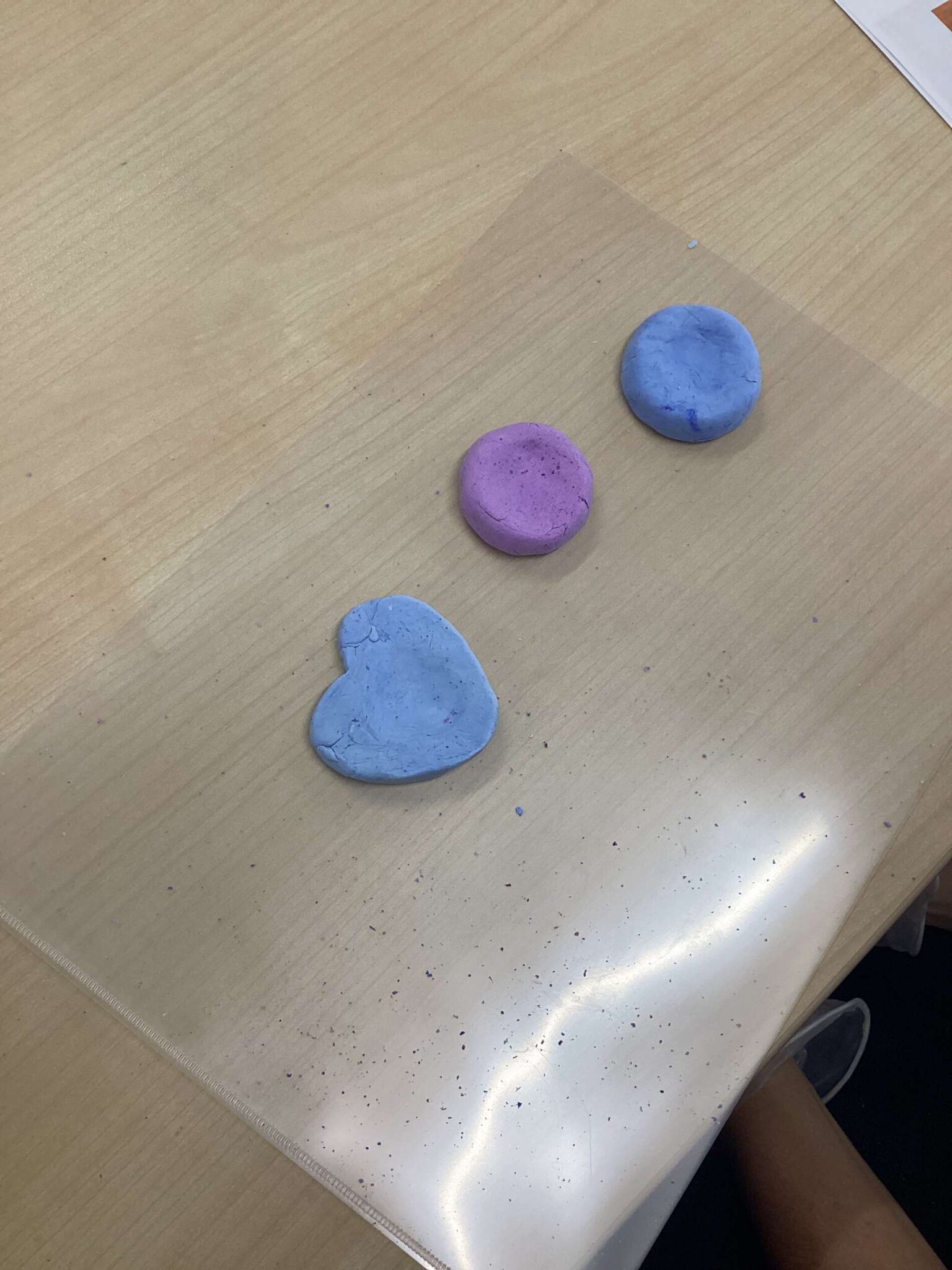Colored clay blobs (purple, blue, and light blue) placed on a wooden table during a craft activity.