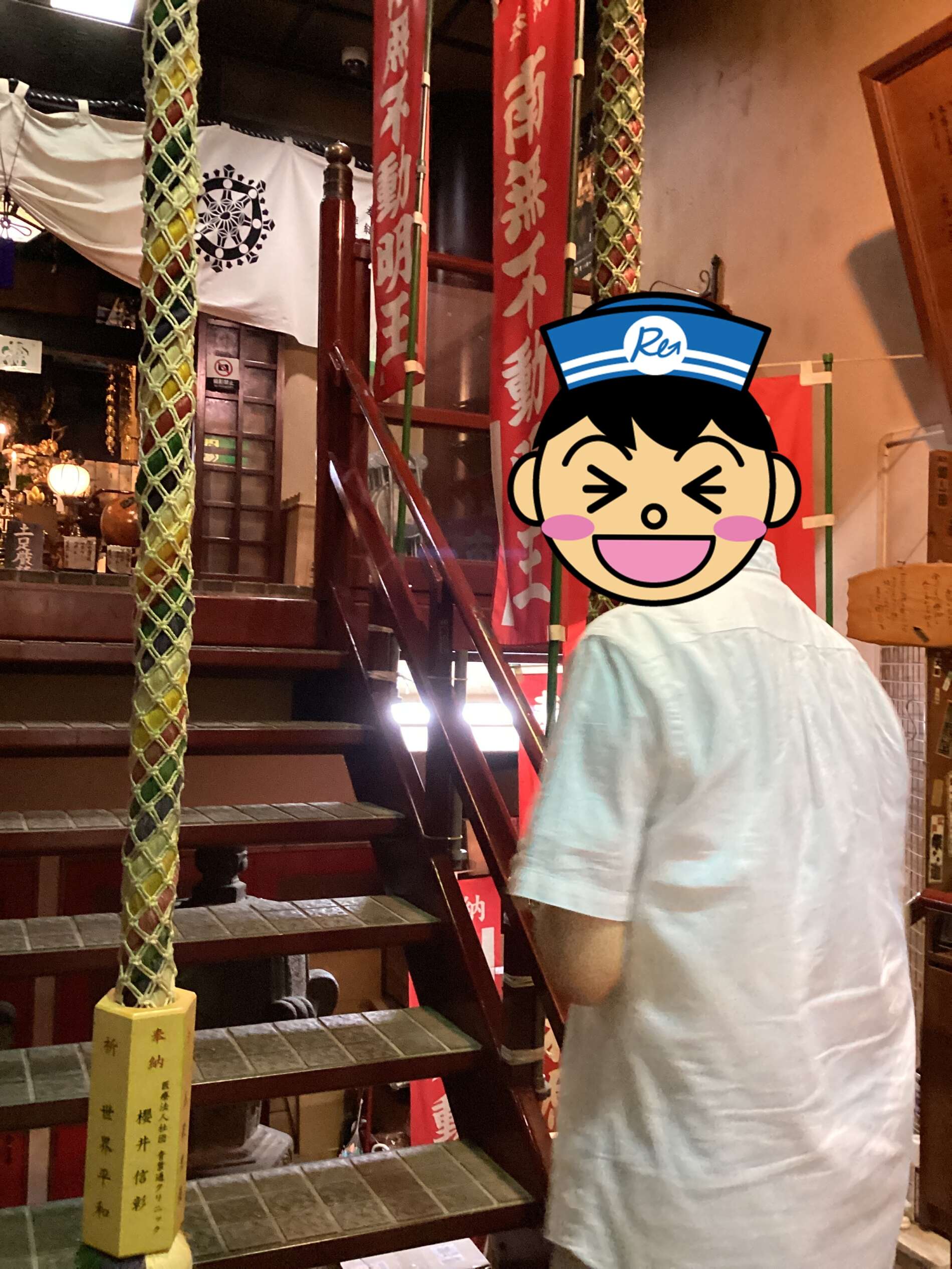 Man in a light shirt near a shrine stairway with red banners and ceremonial rope in a dimly lit interior.