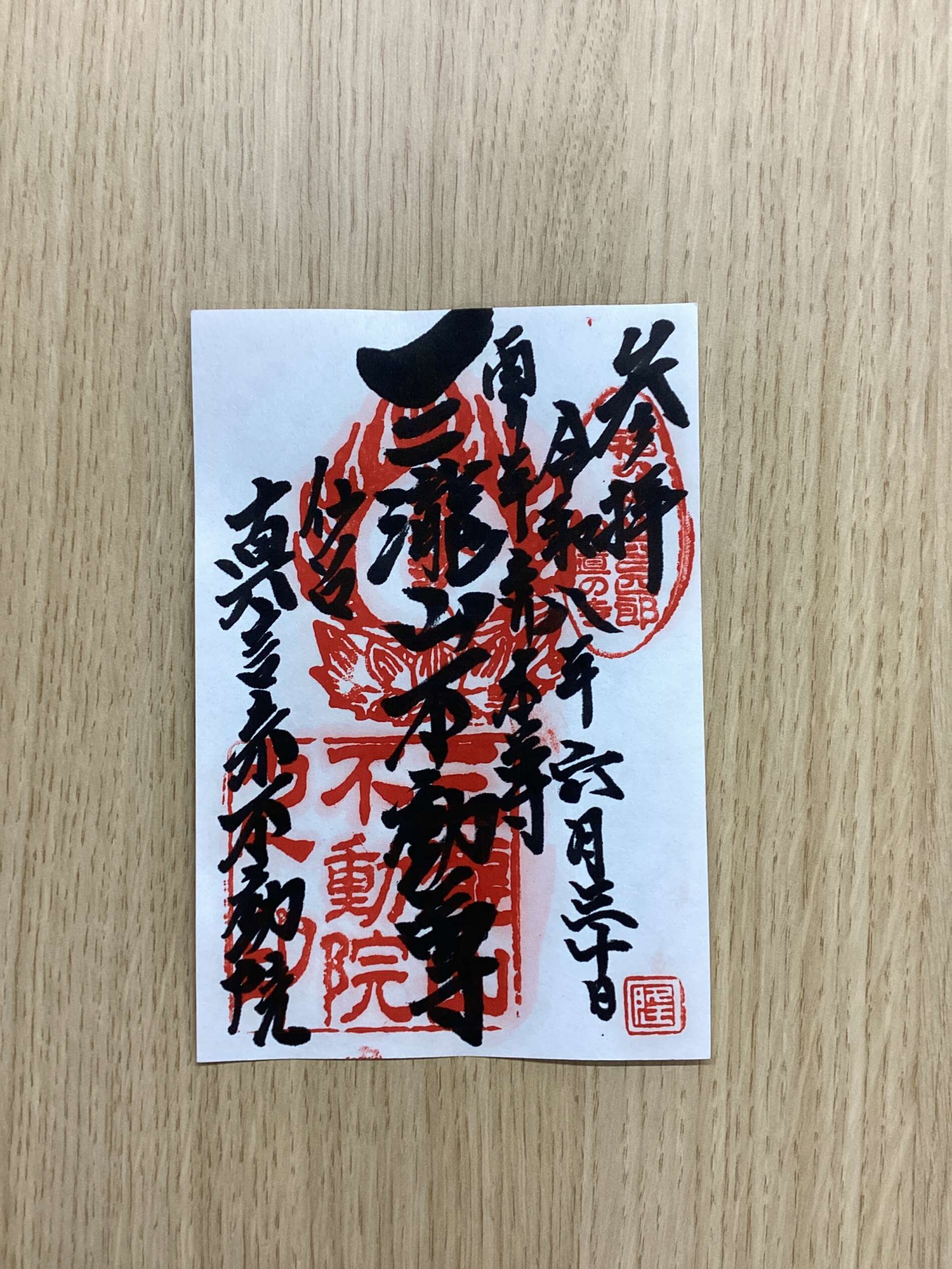White paper with dense black Japanese calligraphy overlaid on red seals, placed on a wooden surface (close-up).