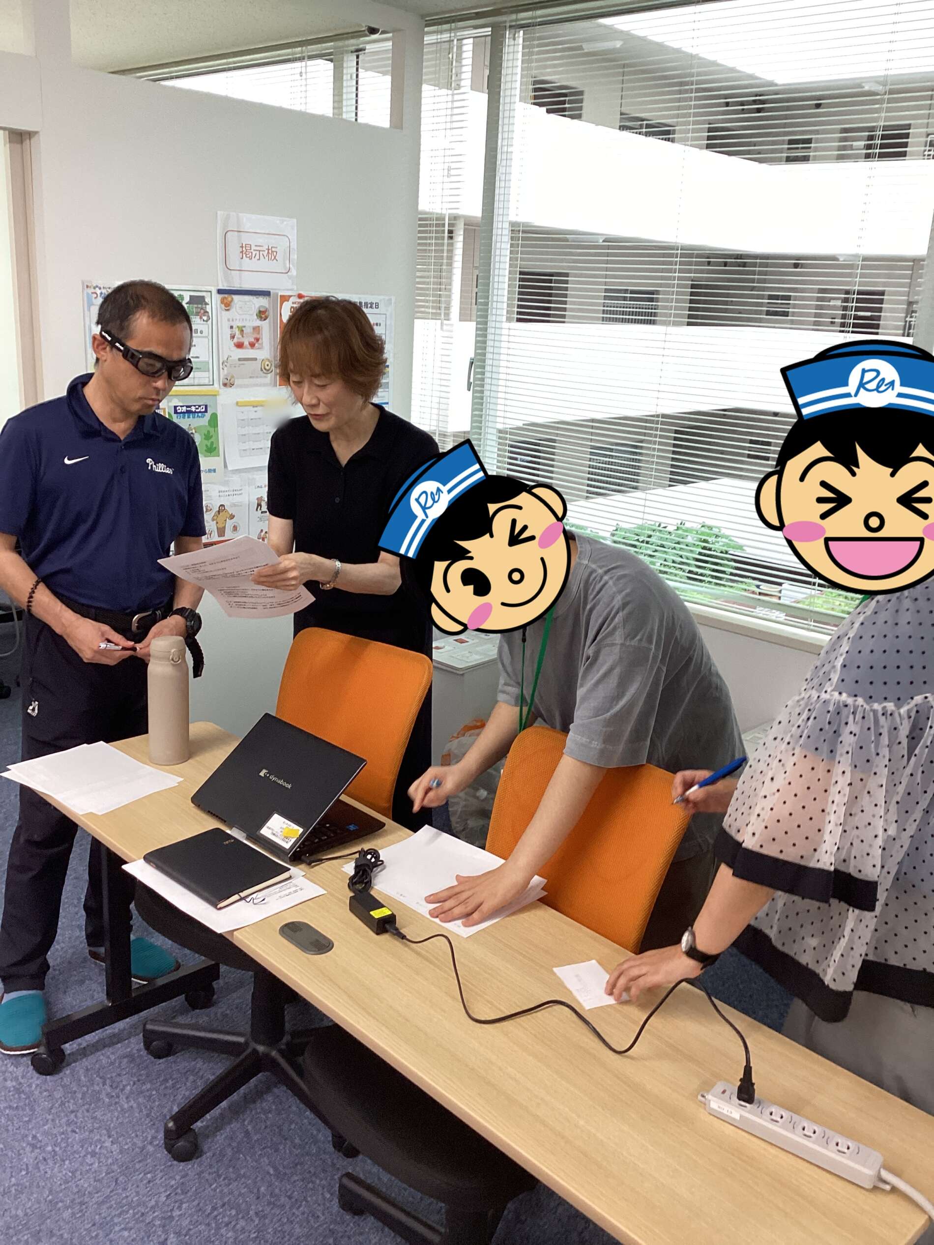Two people standing at a desk, reviewing documents; laptop, papers, and a water bottle on the table in an office setting.