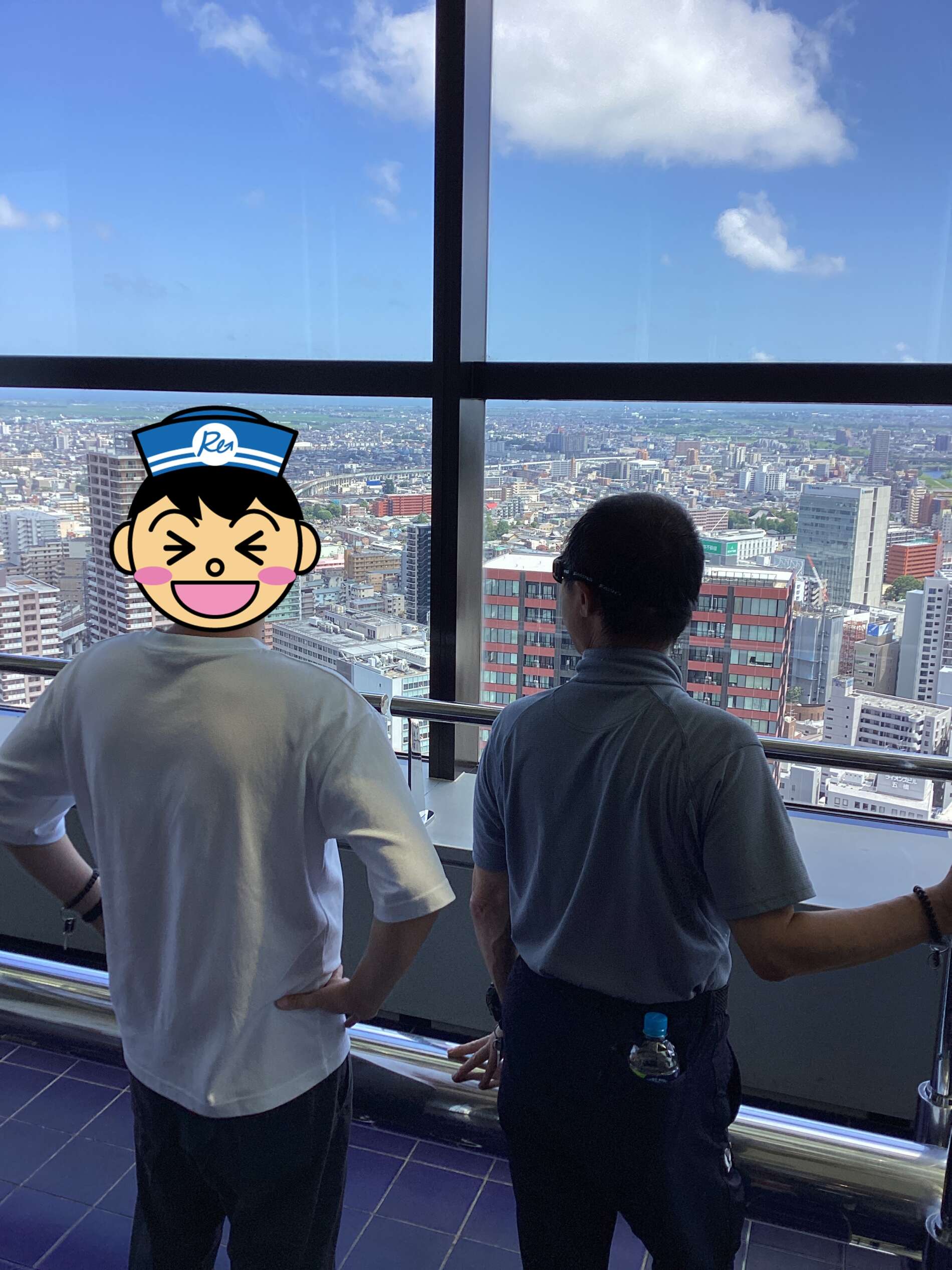 Two people stand at a high observation deck, looking out over a city skyline through large glass panels.