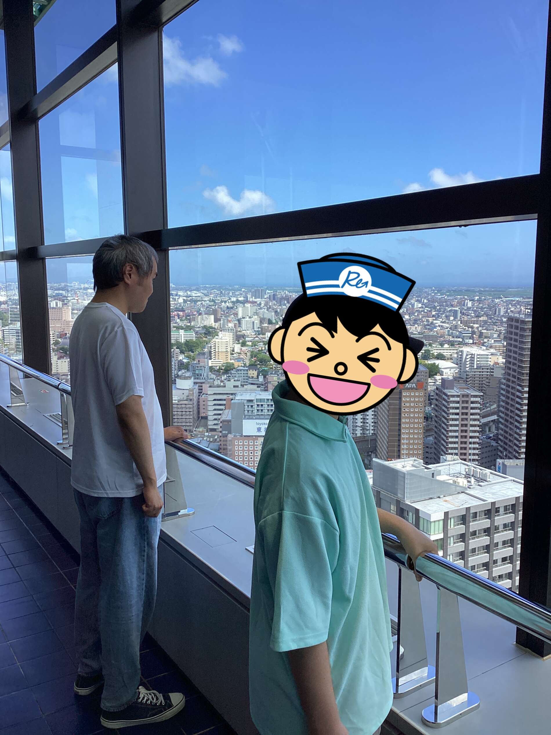 Two visitors stand at an indoor observation deck, looking out over a cityscape through large glass windows.
