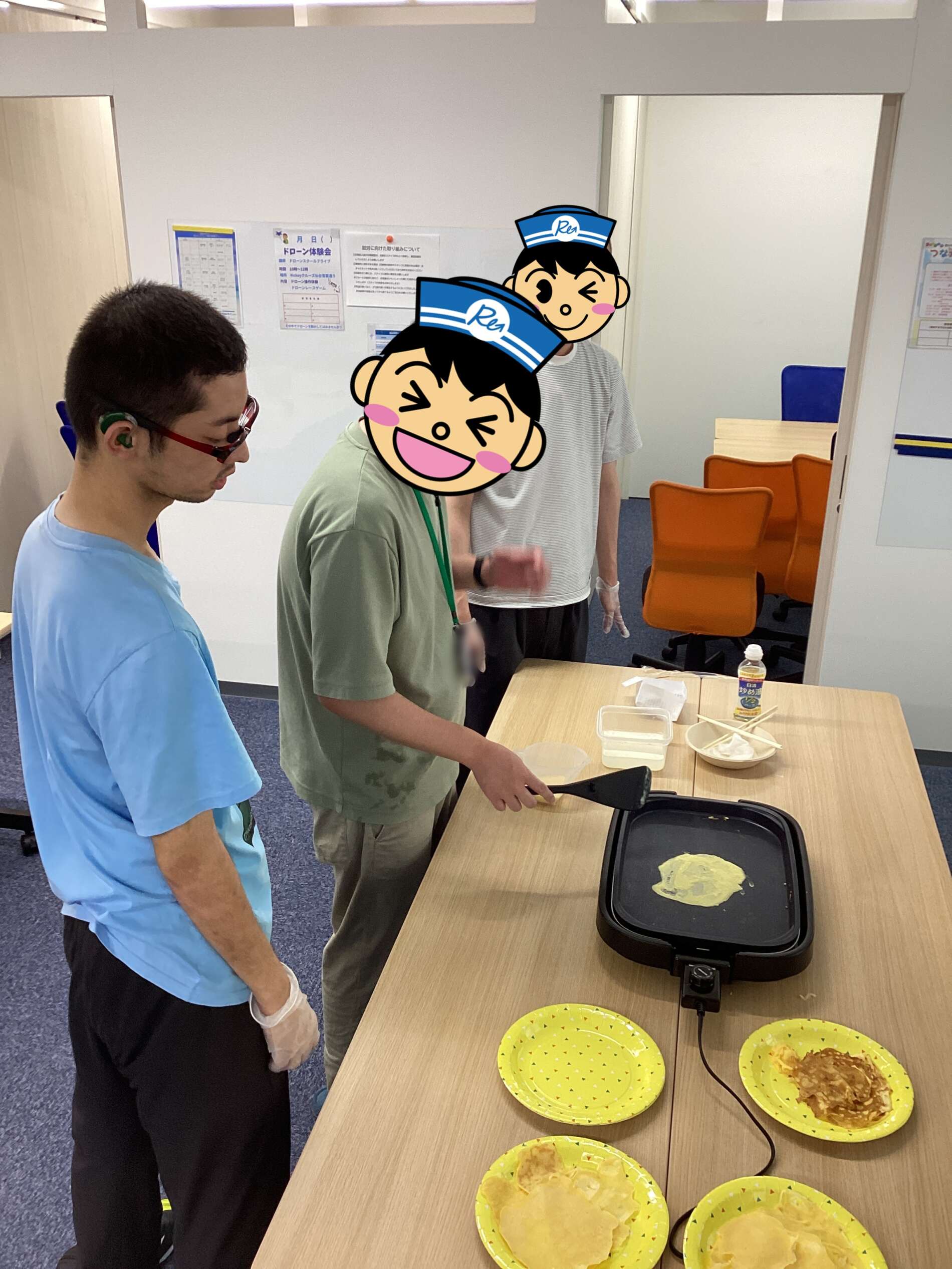People cooking pancakes on a portable griddle at a table, with yellow plates of tortillas nearby.
