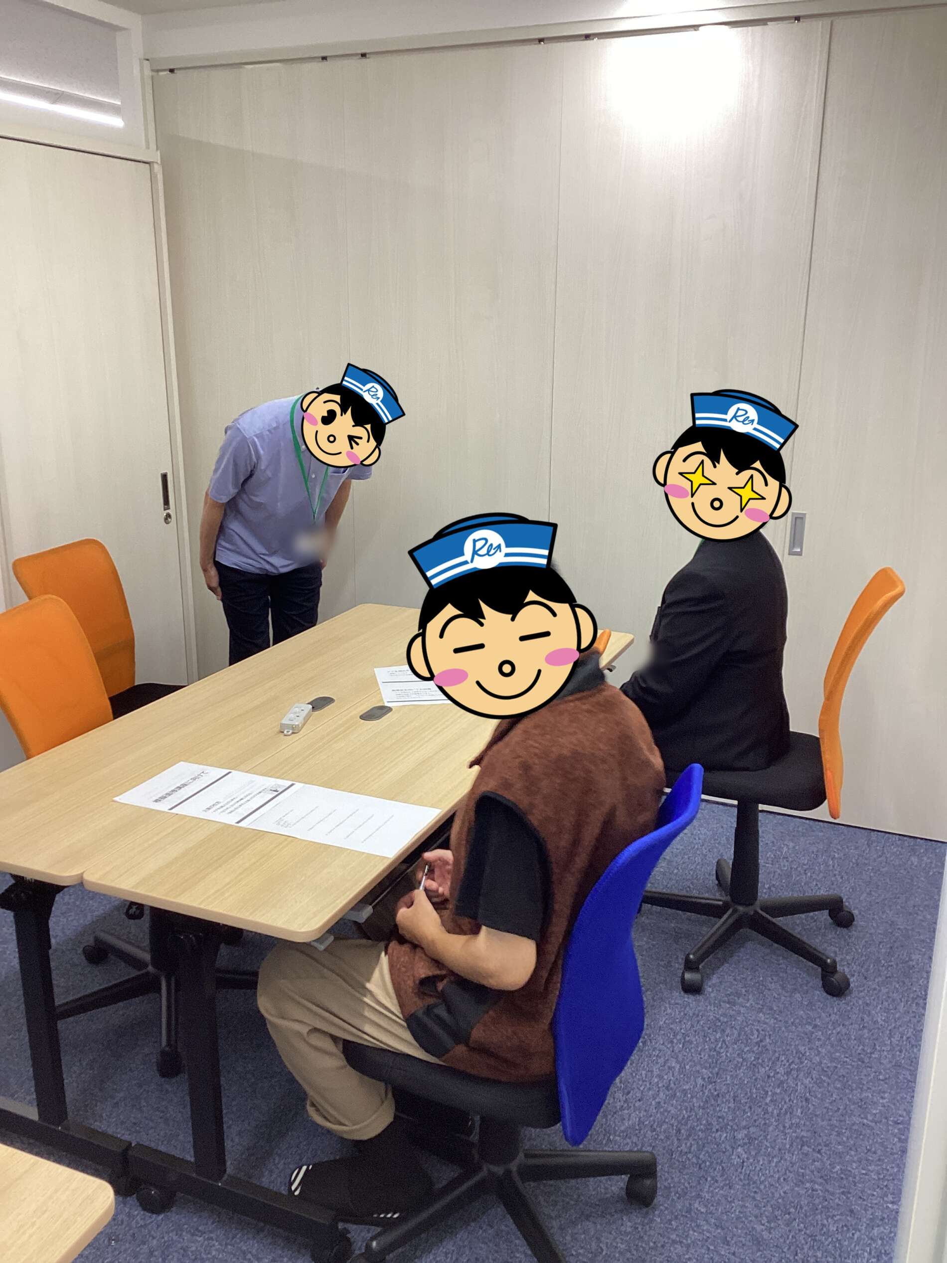 Four people around a rectangular table in a small meeting room; one person stands and looks at documents while three others sit, chairs in blue and orange, faces covered by cartoon avatars.