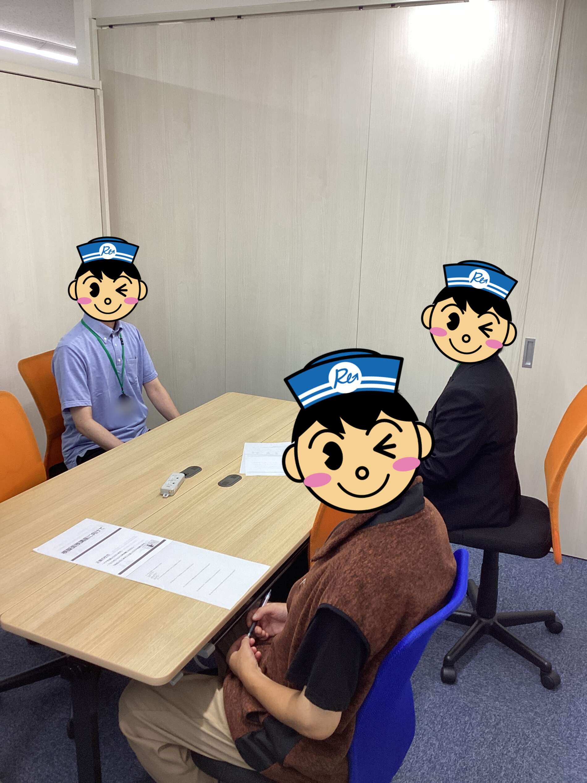 People sit around a conference table with papers, a remote, and notes on the desk in a small meeting room.